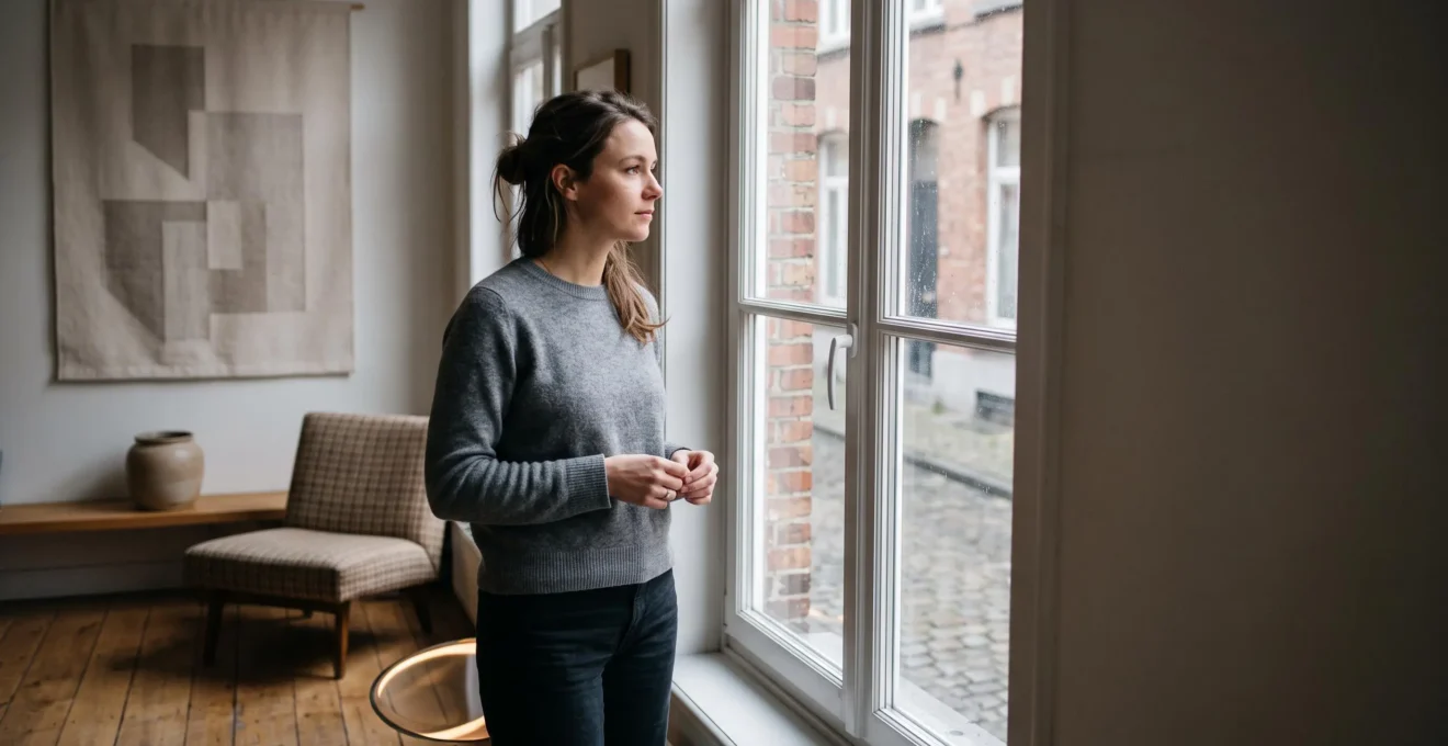 Silhouette d'une femme pensive près d'une fenêtre dans une maison bruxelloise, illustrant les variations naturelles du désir au fil du cycle menstruel